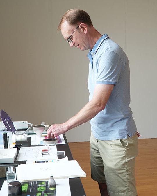 man with short sleeve shirt and glasses looking at items on a table