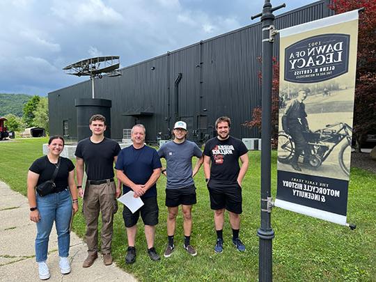 group of five people standing next to a sign