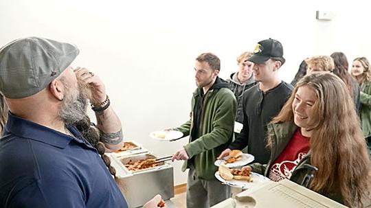 man with beard eating a crawfish as a female student looks on